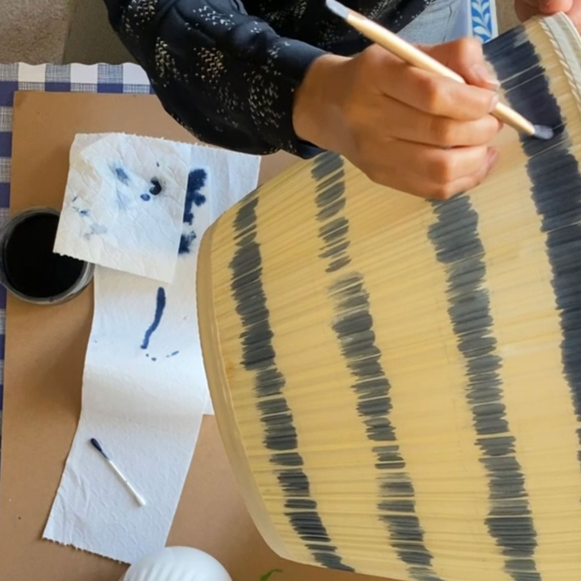 Woman painting blue stripes onto neutral lamp shade