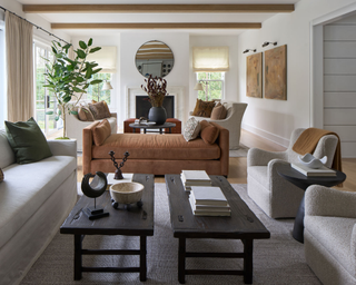 Modern living room space two vintage coffee tables between neutral couches and a burnt orange lounge chair positioned in front of dining space in the background