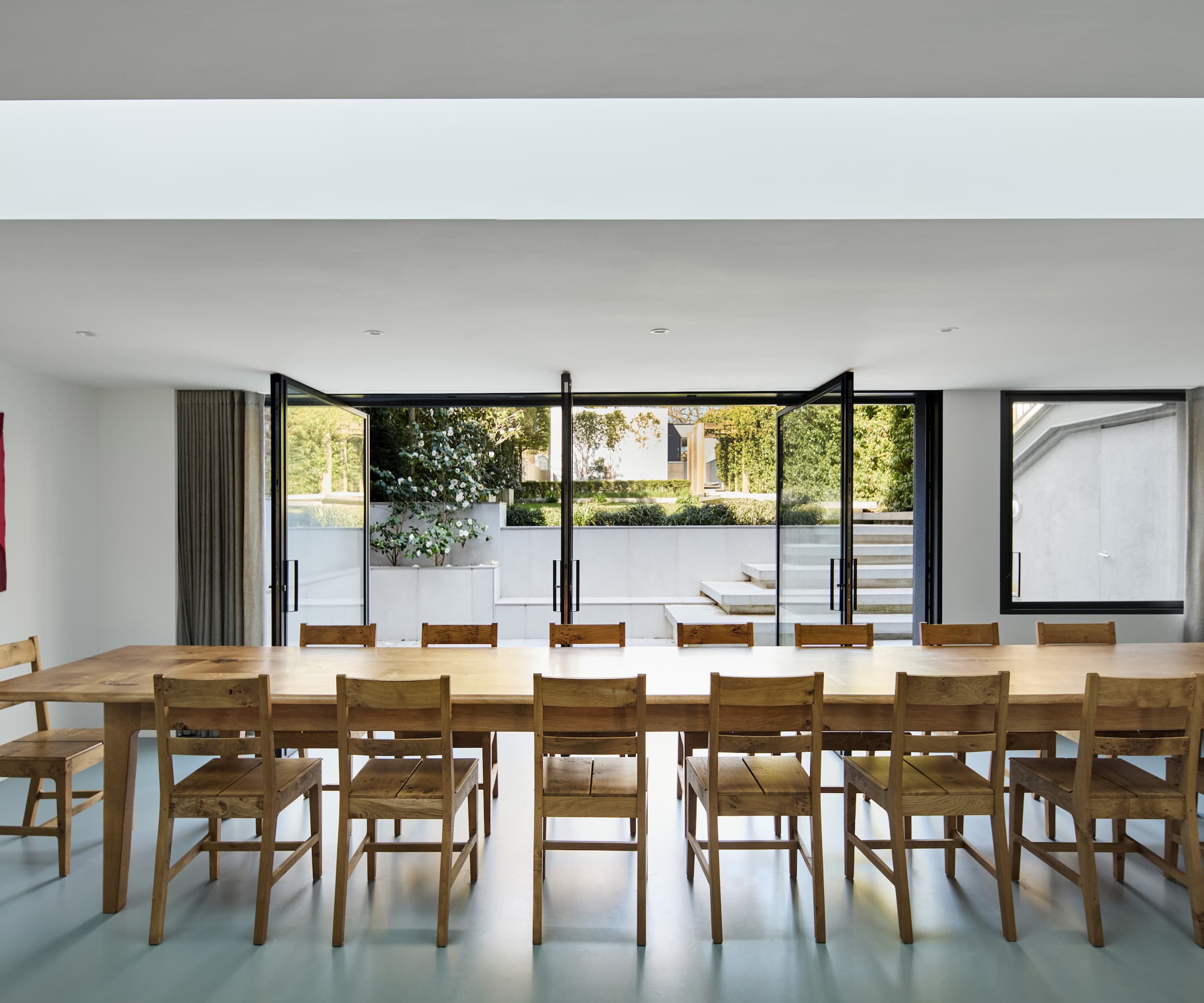 A long wooden dining table leading to double bifold doors and a patio area