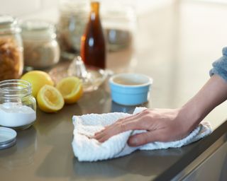 Woman cleaning a kitchen worktop with natural cleaning products lemon, bicarbonate of soda and vinegar