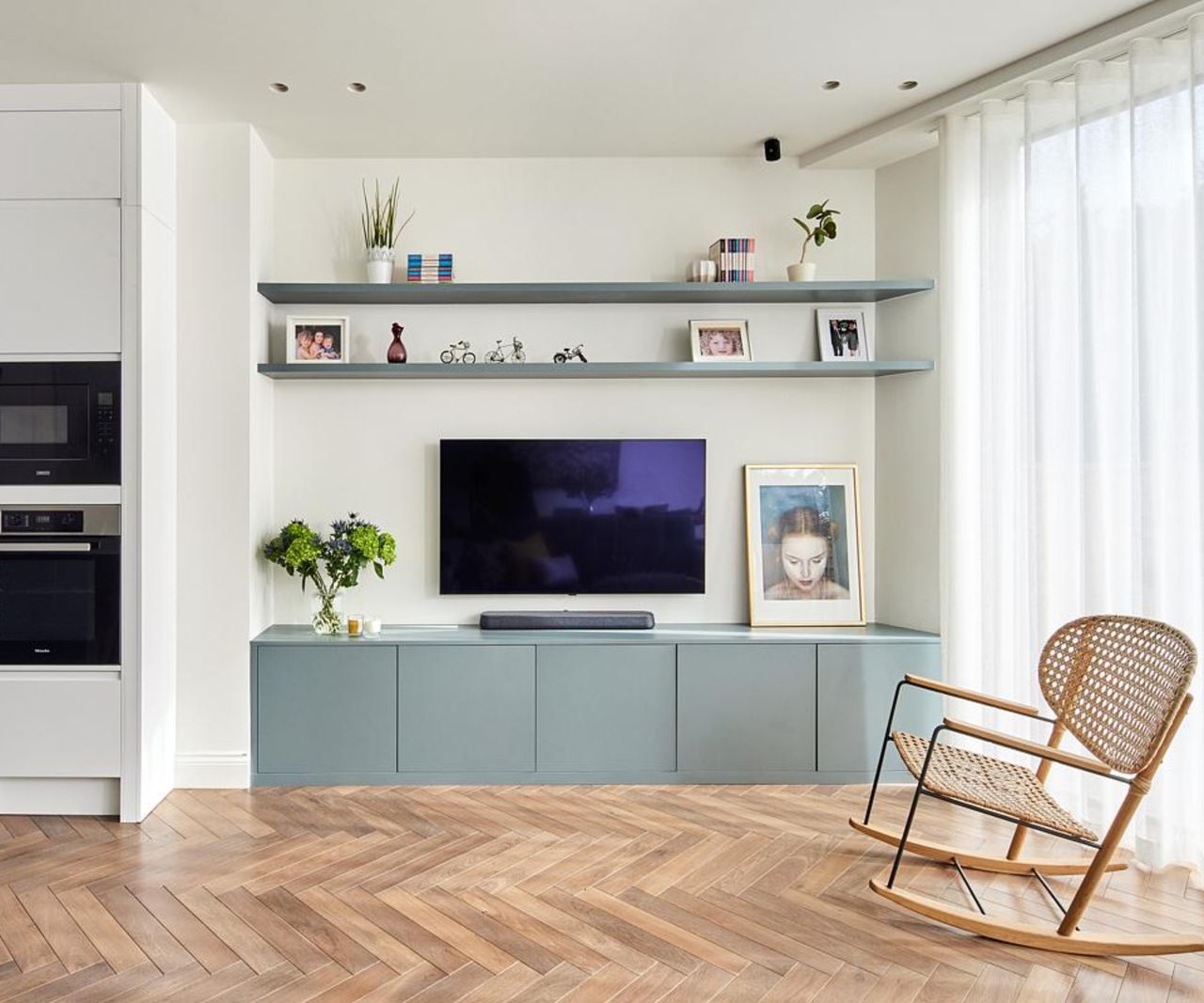inside of living room extension showing media wall with blue units and shelves, wooden floor, skylight above dining table and white built in shelving