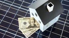 100 dollar bills inside of a house positioned on top of a solar cell panel 