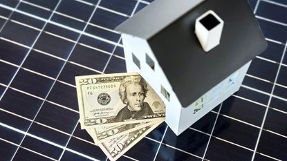 100 dollar bills inside of a house positioned on top of a solar cell panel 