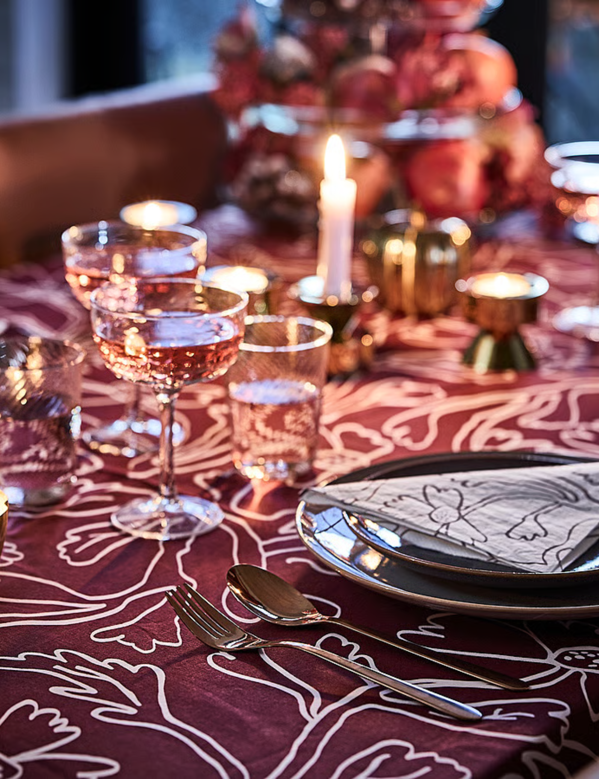 Richly layered fall tablescape featuring botanical-motif oxblood table linens, faceted champagne coupes, and brass candlesticks.