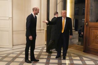 Donald Trump gesturing to Prince William with his hand in front of a large door with a column