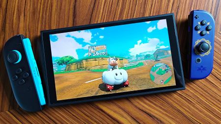 Nintendo Switch 2 with left Joy-Con attached and original Zelda: Skyward Sword Joy-Con on right and Mario Kart World gameplay on screen.