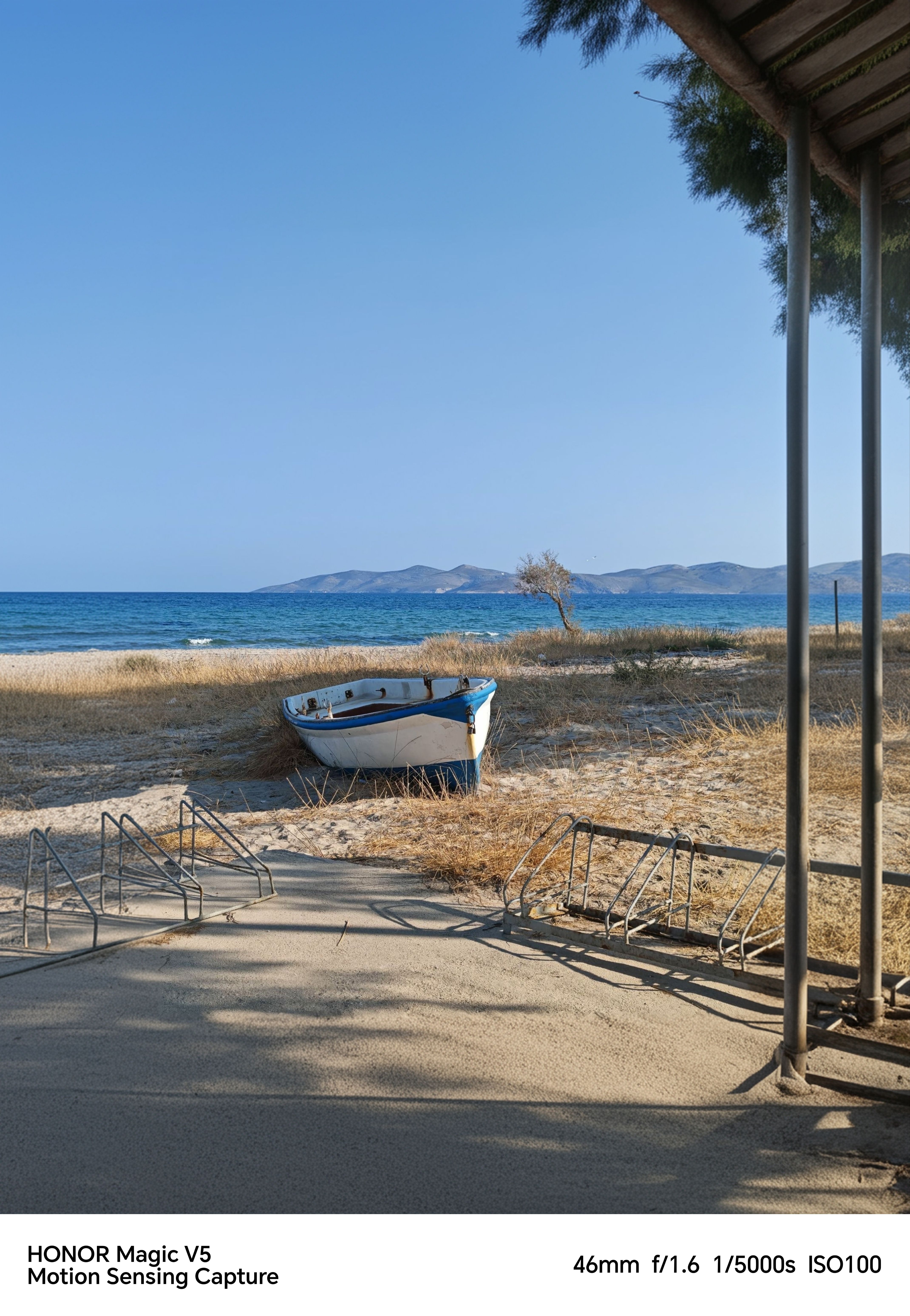 A boat on a beach in front of the ocean with mountains and a blue sky in the background