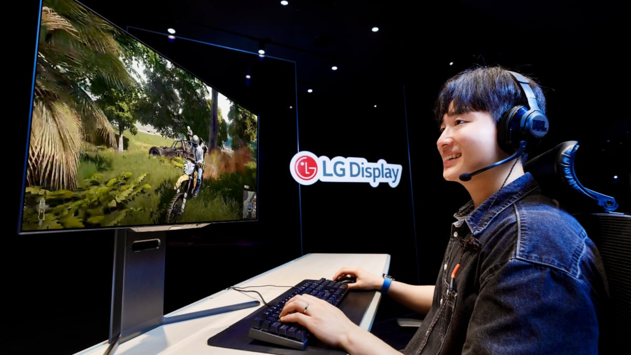 A young man playing a game in front of an LG RGB Tandem OLED gaming monitor