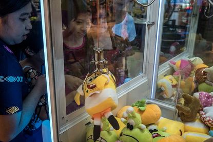 Kids in Malaysia play a claw machine in an arcade.