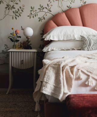A pink bed with white bedding in front of floral wallpaper