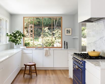 Small kitchen with white cupboards, a white marble backsplash, blue range and large windows