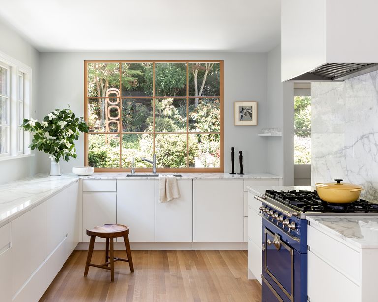 Small kitchen with white cupboards, a white marble backsplash, blue range and large windows