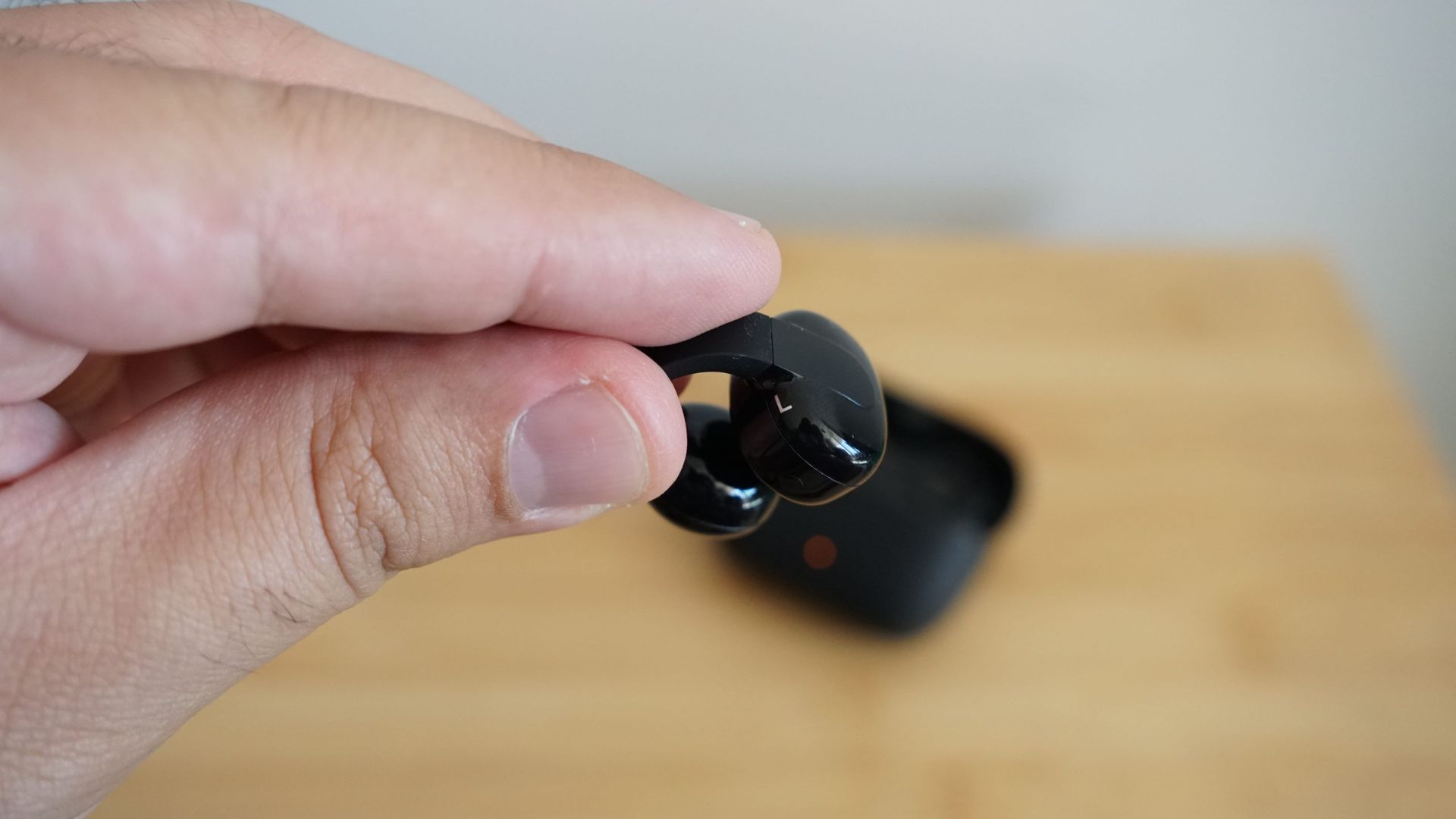 Sennheiser's Accentum Clip held in a hand, over a wooden table, with the case visible