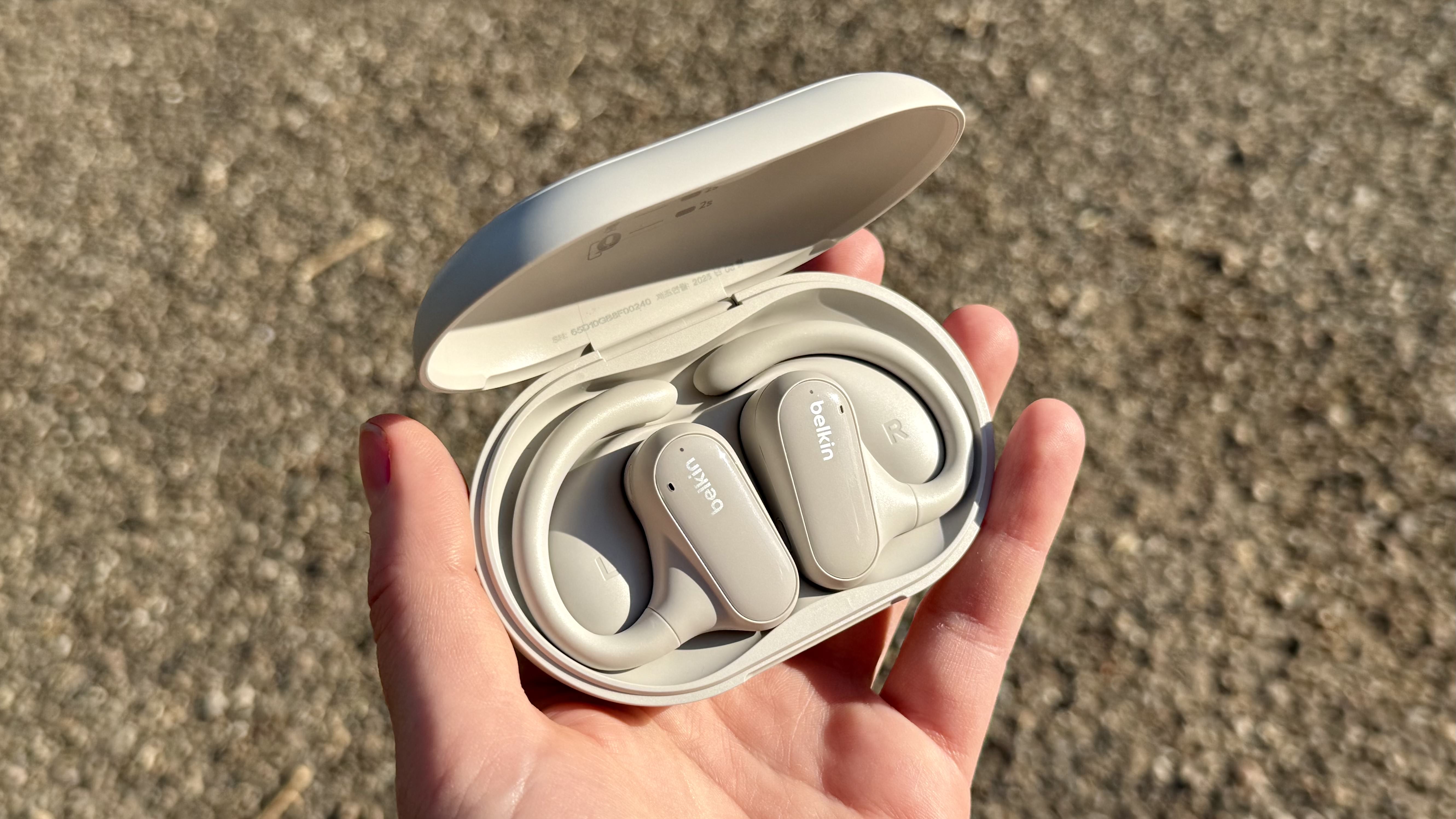 A hand holding the Belkin SoundForm Clear fit buds in their charging case.