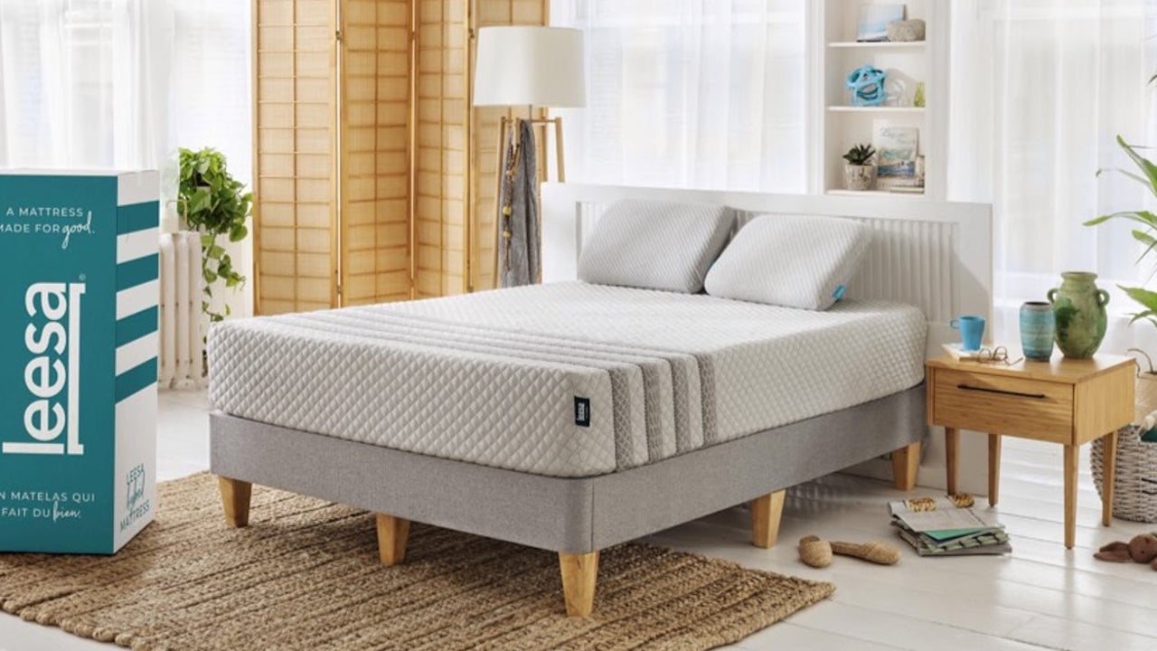 Best memory foam mattress: The Leesa Hybrid sat on a light gray fabric bed base next to a light wooden bedside table and a blue and white Leesa box