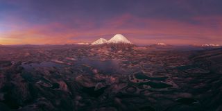 Aerial landscape of snow-capped volcanoes, rugged terrain, and interconnected lakes beneath a vivid purple-orange sunset