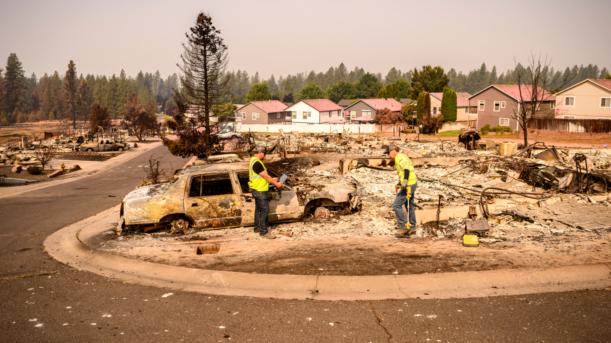 Utility workers help clear obstacles at a burned home during the Old Trails Fire in Spokane, Washington