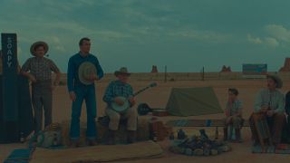 Rupert Friend stands, hat in hand, among a group of people in the desert in Asteroid City.