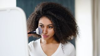 Close-up portrait of young woman with brush indoors at home,applying makeup - stock photo