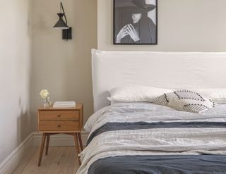 A bed with a white and blue bed sheets, a linen headboard, and a small wooden nightstand