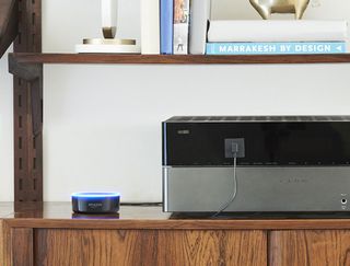 Smart home devices on a wooden shelf below books and ornaments