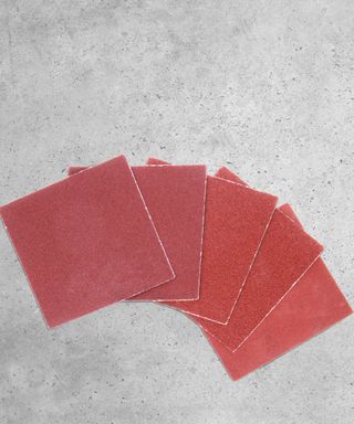 Five red sandpaper squares fanned out onto a gray cement background