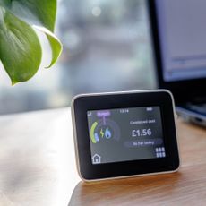 Smart meter on a desk next to a laptop and a plant