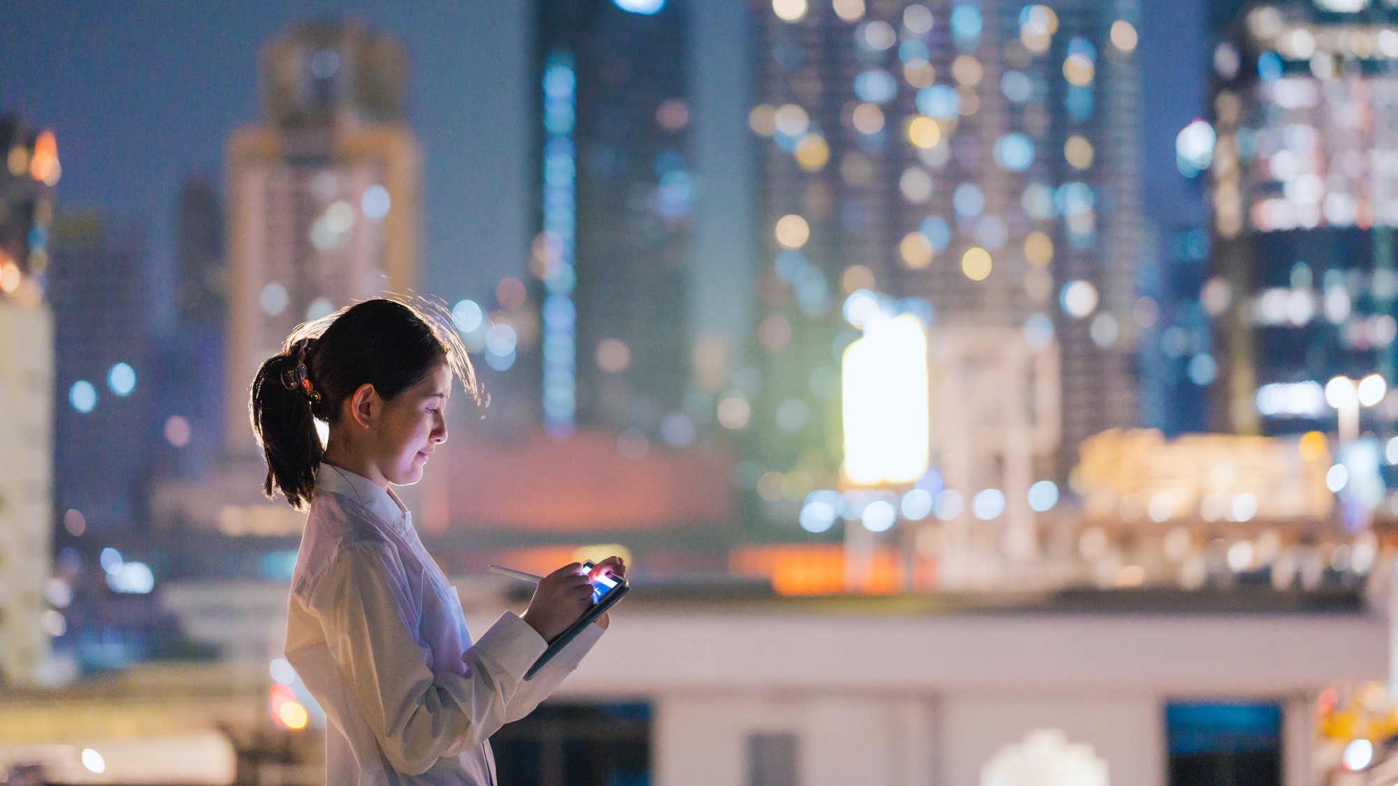 Woman working on a digital tablet in front of a blurry cityscape at night