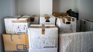 A white painted room filled with taped up cardboard boxes of stuff