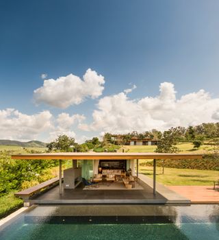 Overlooking part of the house complex with an open plan outdoor area and swimming pool, surrounded by a green landscape.