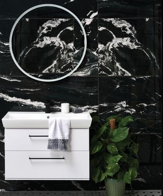 A bathroom backsplash idea with large format black marble-effect porcelain tiles and white sink and round mirror