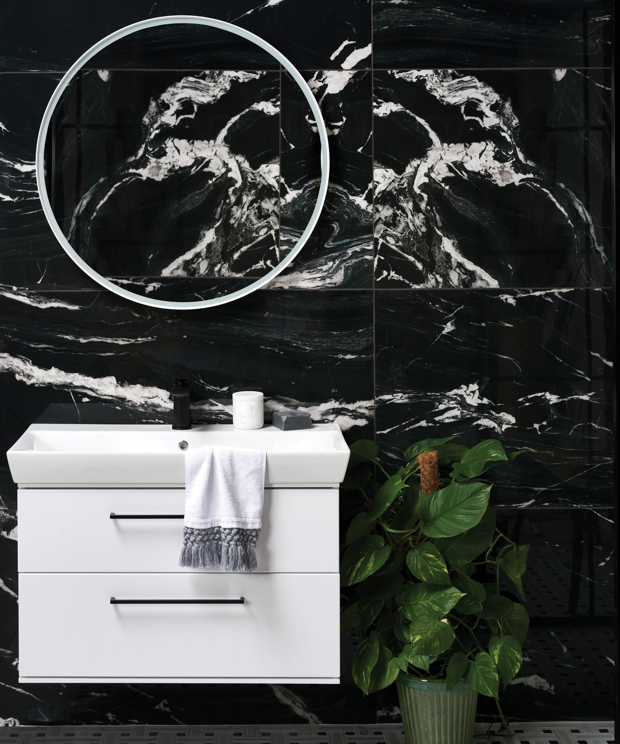 A bathroom backsplash idea with large format black marble-effect porcelain tiles and white sink and round mirror