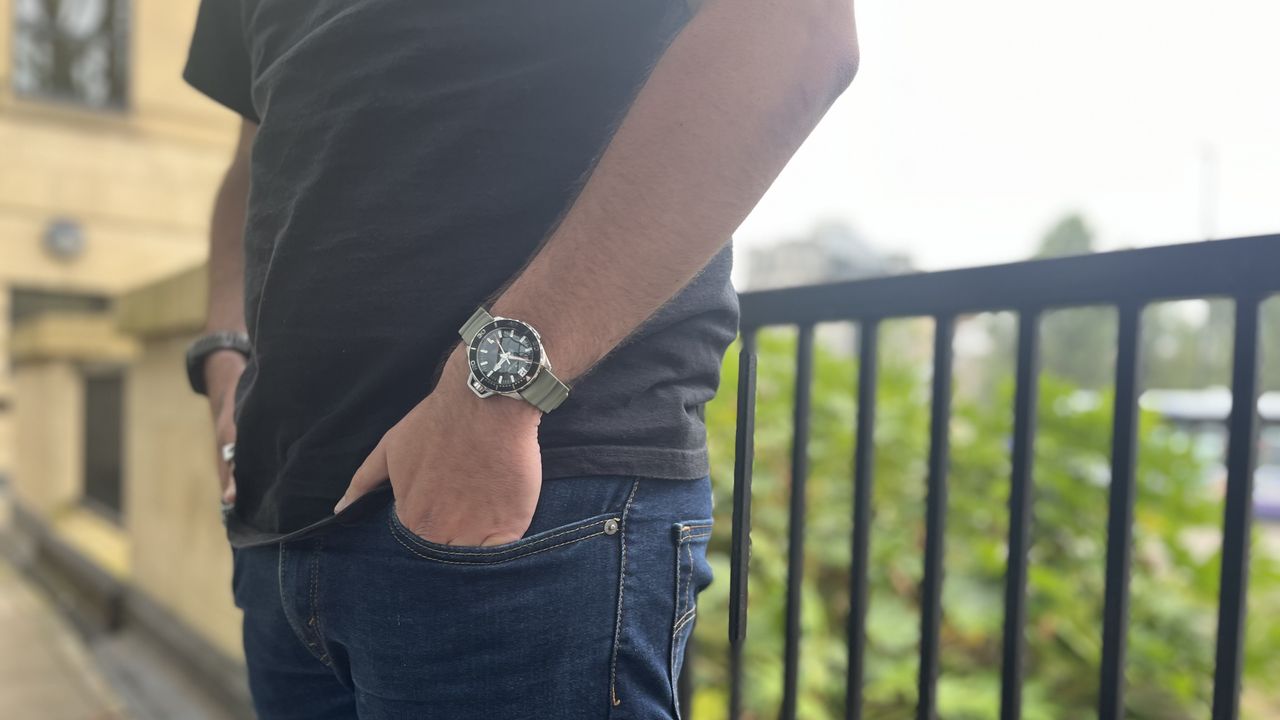 The Hamilton Khaki Navy Frogman with a black dial and a green rubber strap worn on a wrist in front of a green background