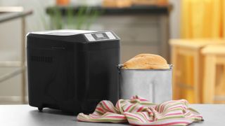 A bread machine next to a loaf of bread on the edge of a counter