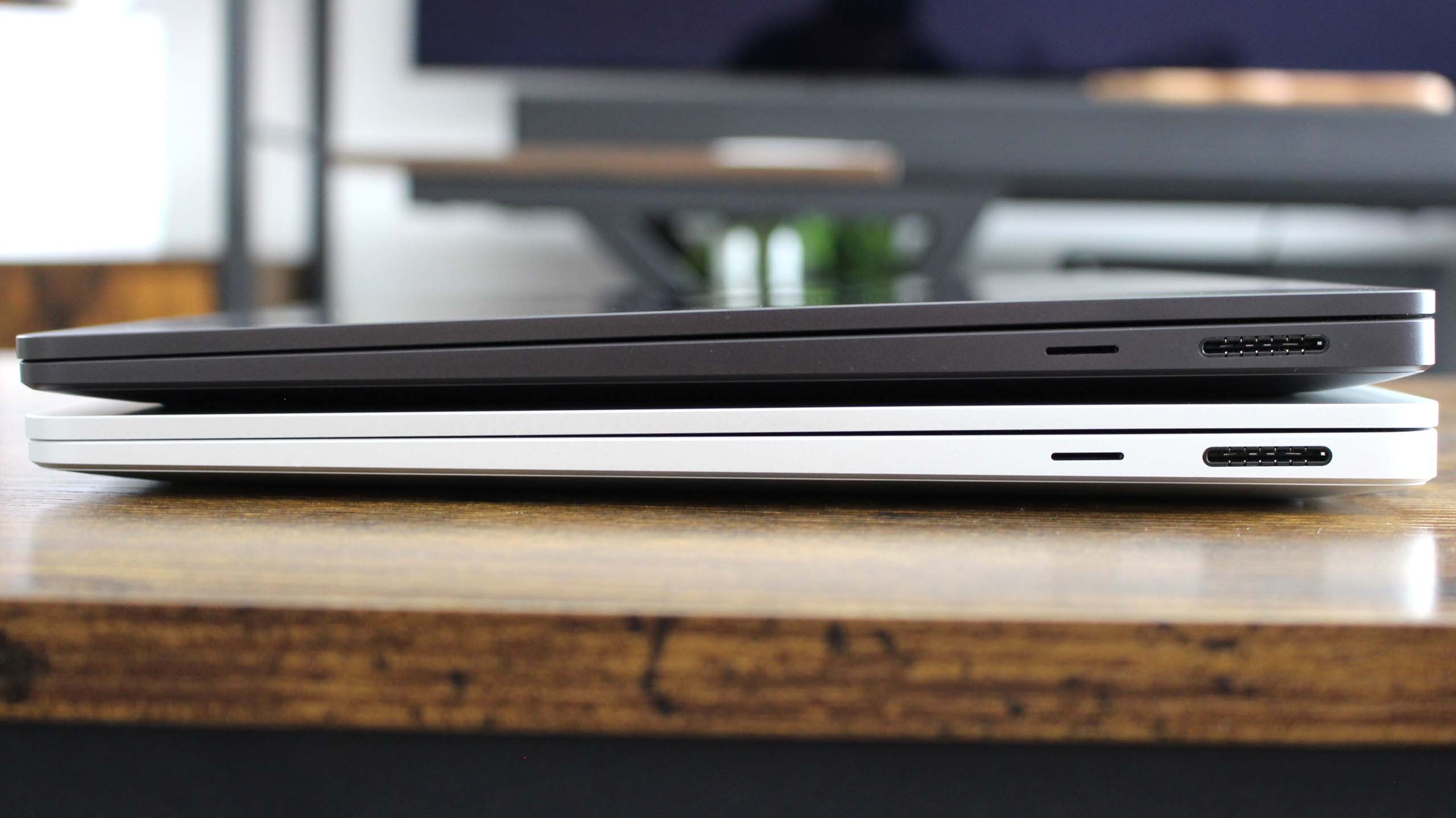 Two Surface Laptop models stacked with black and silver models on a wooden table