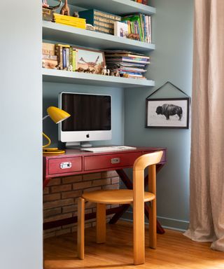 Red desk against blue walls with retro wooden chair and floating shelves