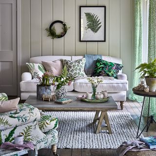 A country living room with wall panels, artwork and floral cushions