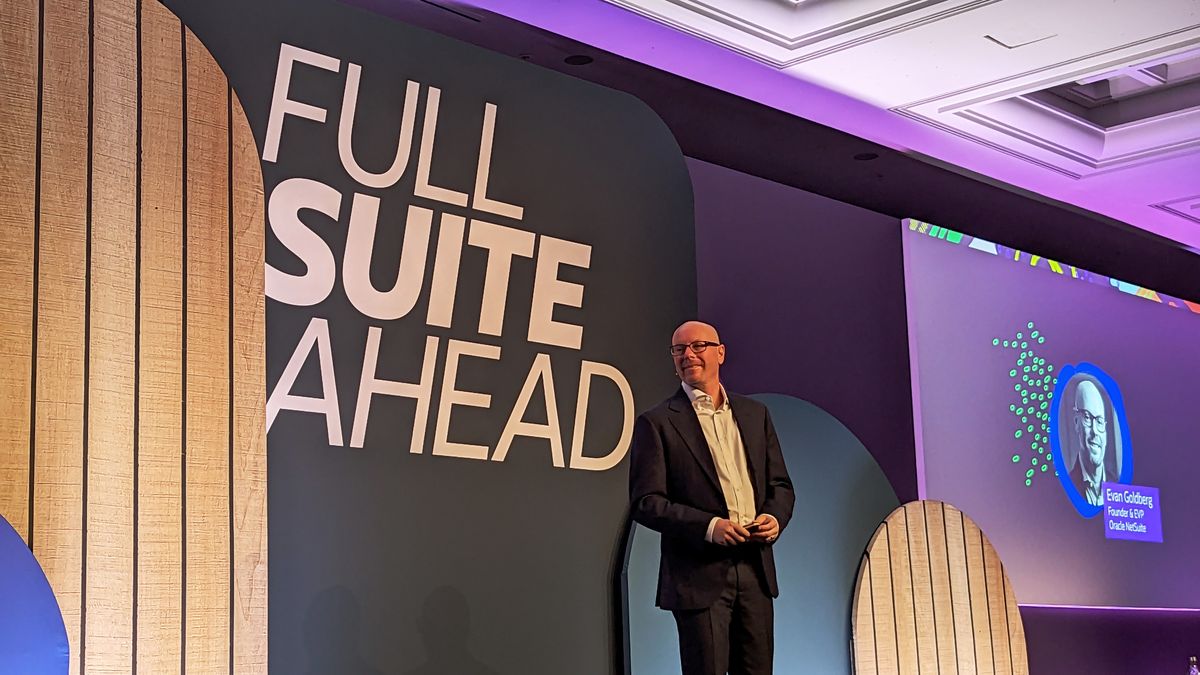 Evan Goldberg, founder and EVP, Oracle NetSuite standing in front of a sign that says &amp;#039;FULL SUITE AHEAD&amp;#039; on a stage, lit by purple lighting