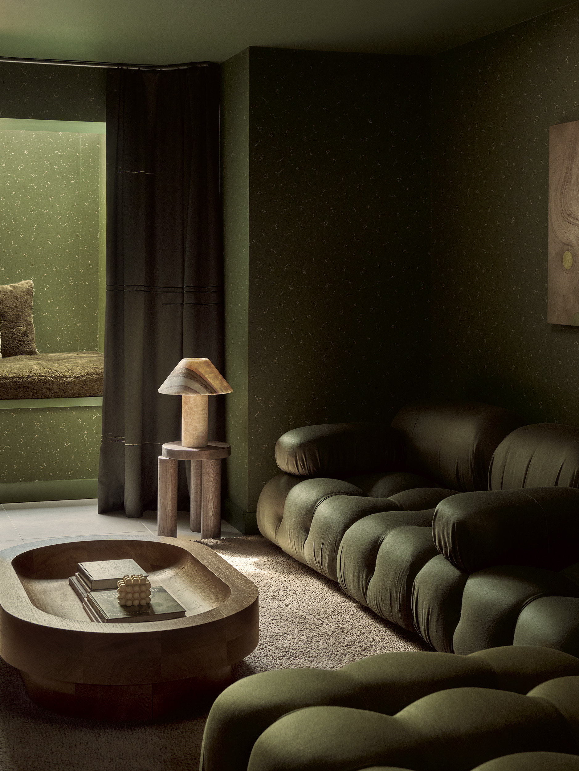 green living room with green corner sofa, timber round coffee table, stool with lamp, green spotty wallpaper with alcove seating and skylight