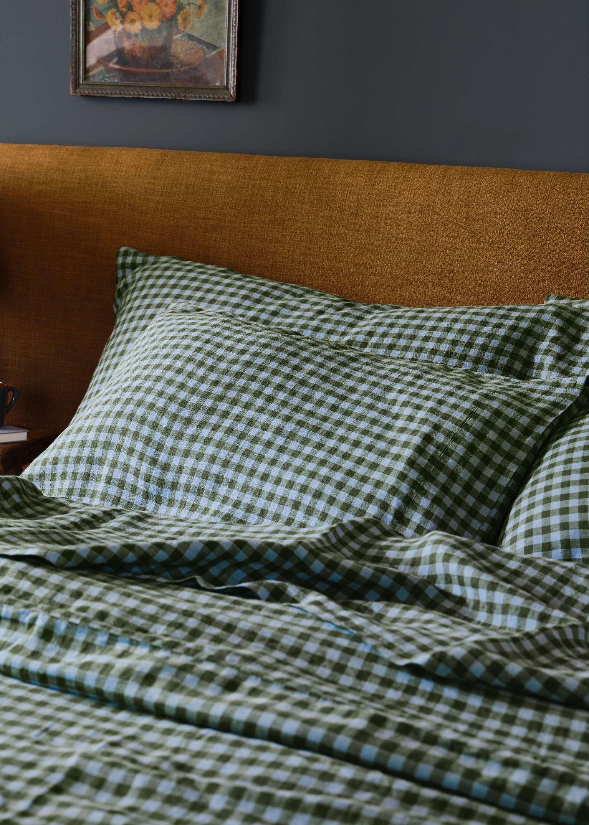 A bed with blue gingham bedding and a mustard headboard.