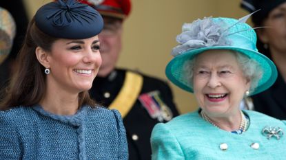 Queen Elizabeth II wears a turquoise green outfit and matching hat while smiling at Kate Middleton, who wears a blue suit