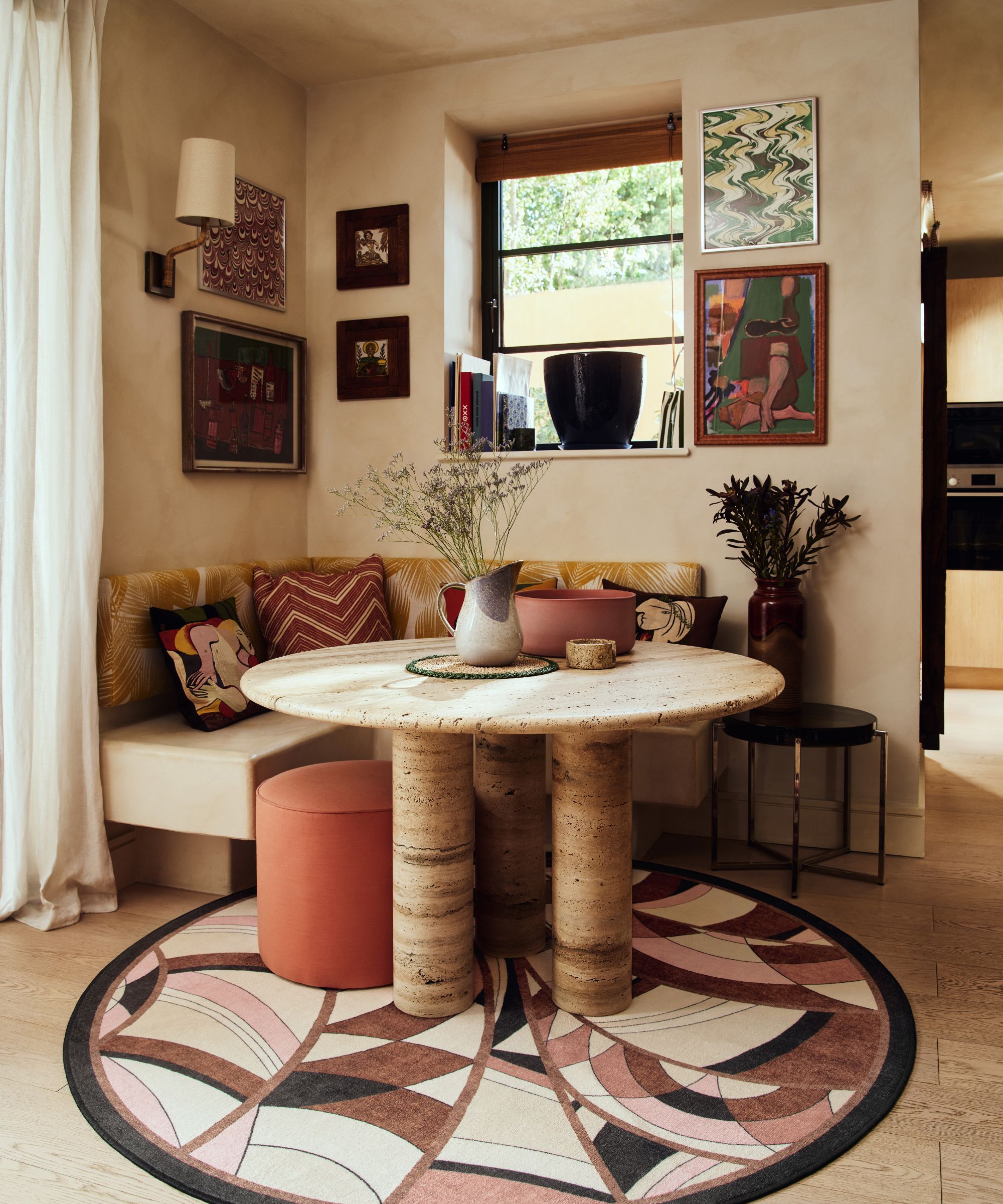 earthy limewashed breakfast nook in the corner of a dining room with a travertine round table, bench seat, and a round patterned rug