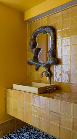 a yellow tiled bathroom with an artistic mirror