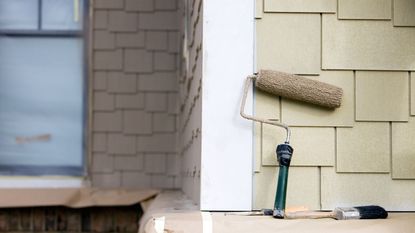 A roller and paint brush against the exterior wall of a house