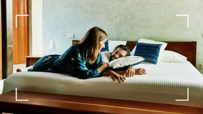 Woman and man laughing on a bed holding a pillow, one of the essentials for the speed bump sex position