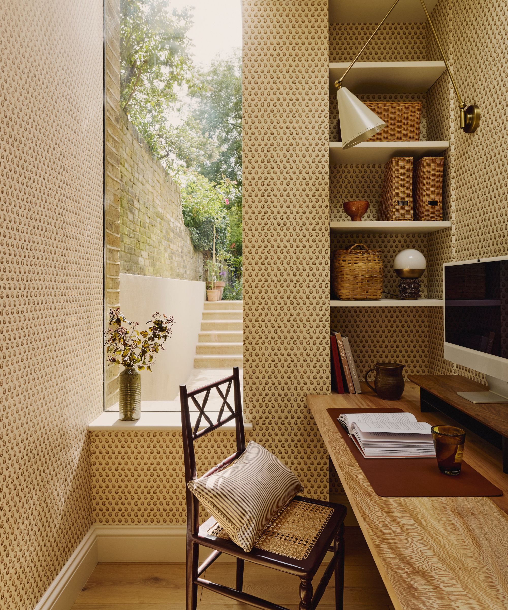 an office area with patterned wallpaper, built-in shelves with storage inside the shelves, and a desk with a book and a computer on top