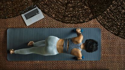 Woman doing 20-minute workout on yoga mat in living room next to open laptop