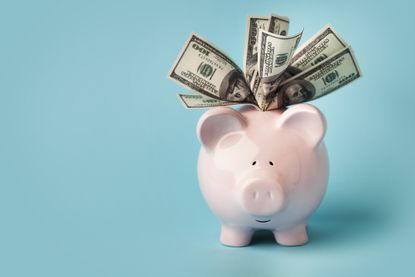 "A smiling pink piggybank stuffed with $100 dollar bills, on blue background with copy space.You may also like:"