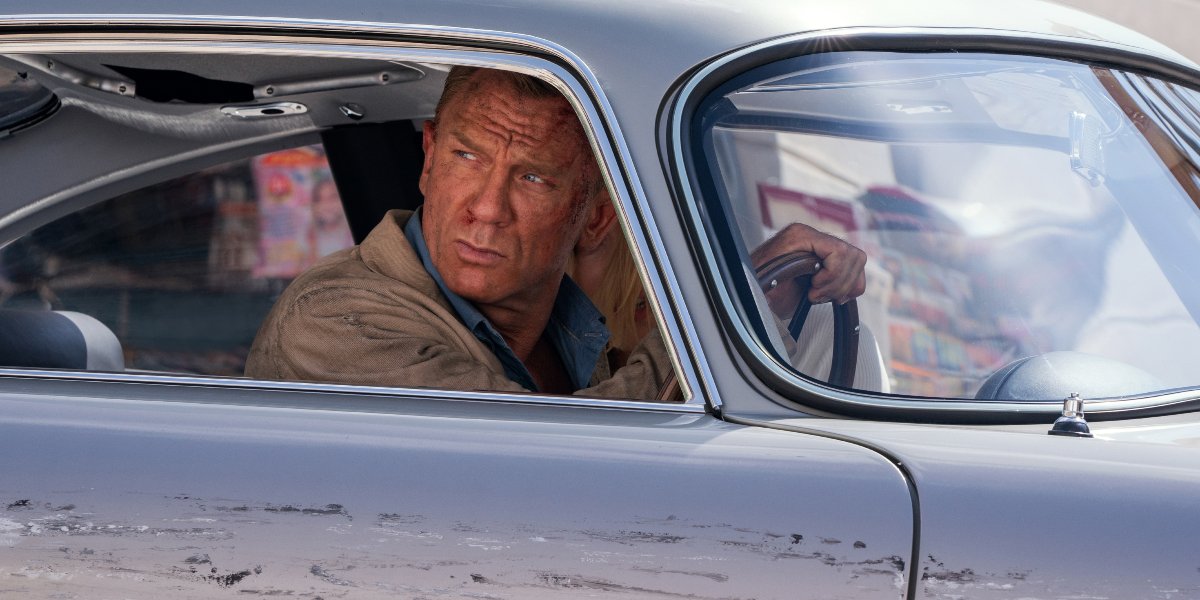 Daniel Craig glares while driving a damaged DB5 in No Time To Die.