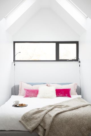 Bedroom in a loft conversion with high vaulted ceiling, white bed covers and bright pink cushions